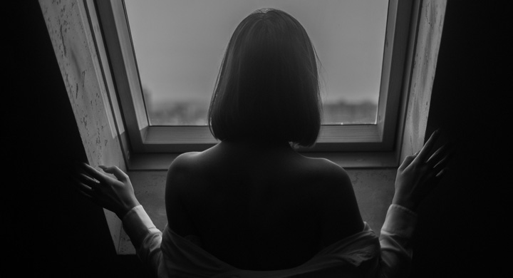 A woman looking sad gazing out of a window in a home